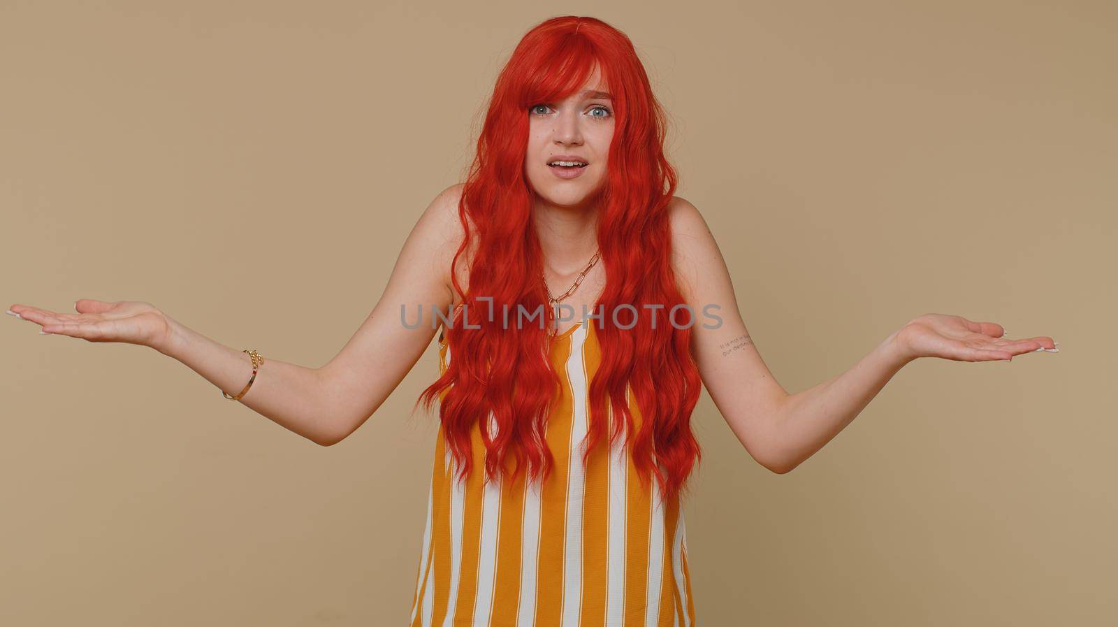 What Why. Sincere irritated redhead woman raising hands in indignant expression asking reason of failure demonstrating disbelief irritation by troubles. Confused girl isolated on beige wall background