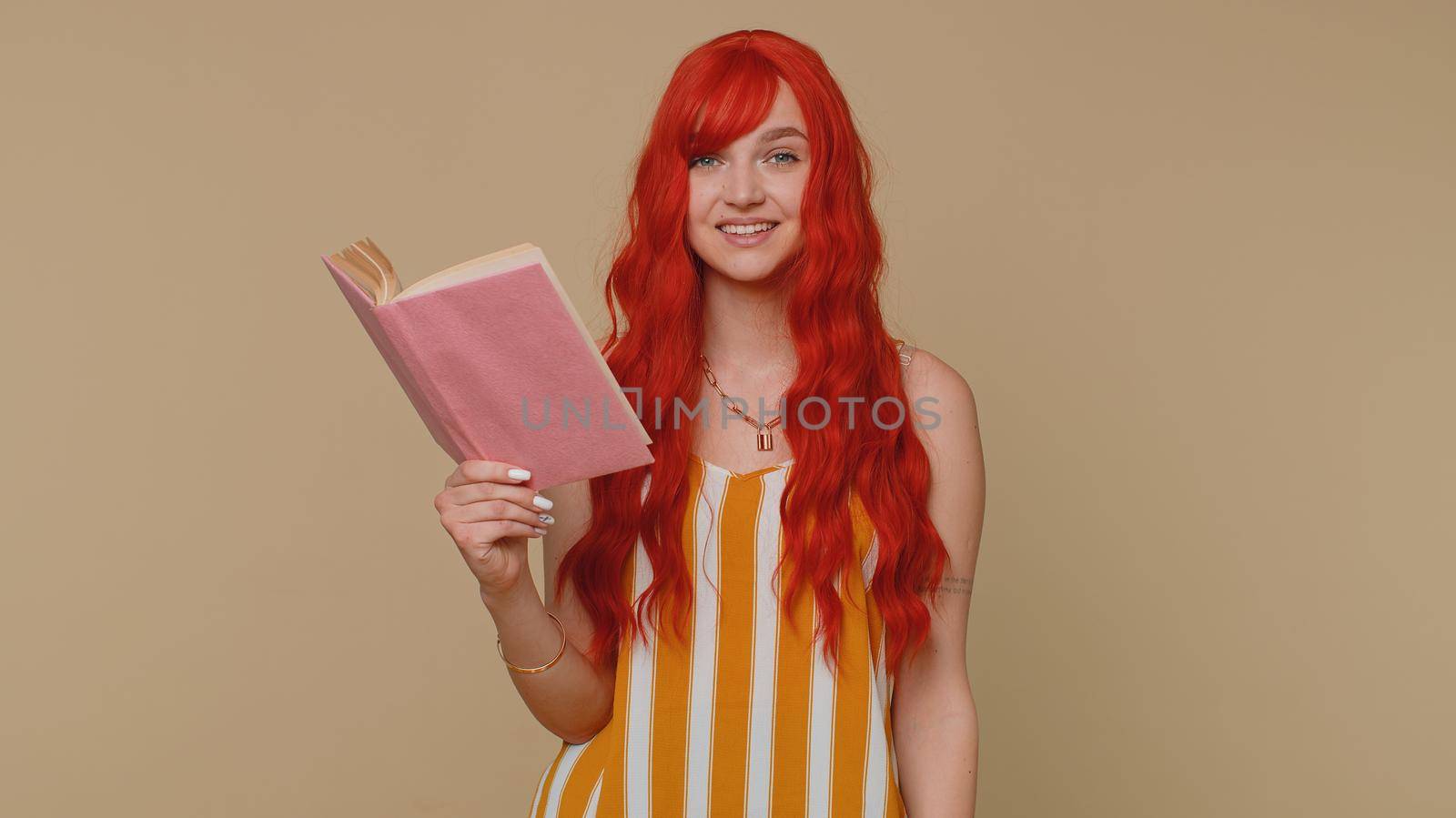 Redhead young woman reading funny interesting fairytale story book, leisure hobby, knowledge wisdom, education learning, study, wow. Red hair ginger girl isolated alone on beige studio wall background