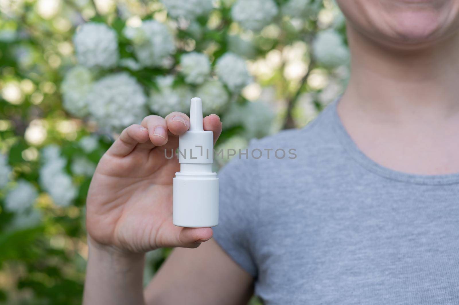 Happy woman demonstrating nasal spray on the background of a blossoming tree. by mrwed54