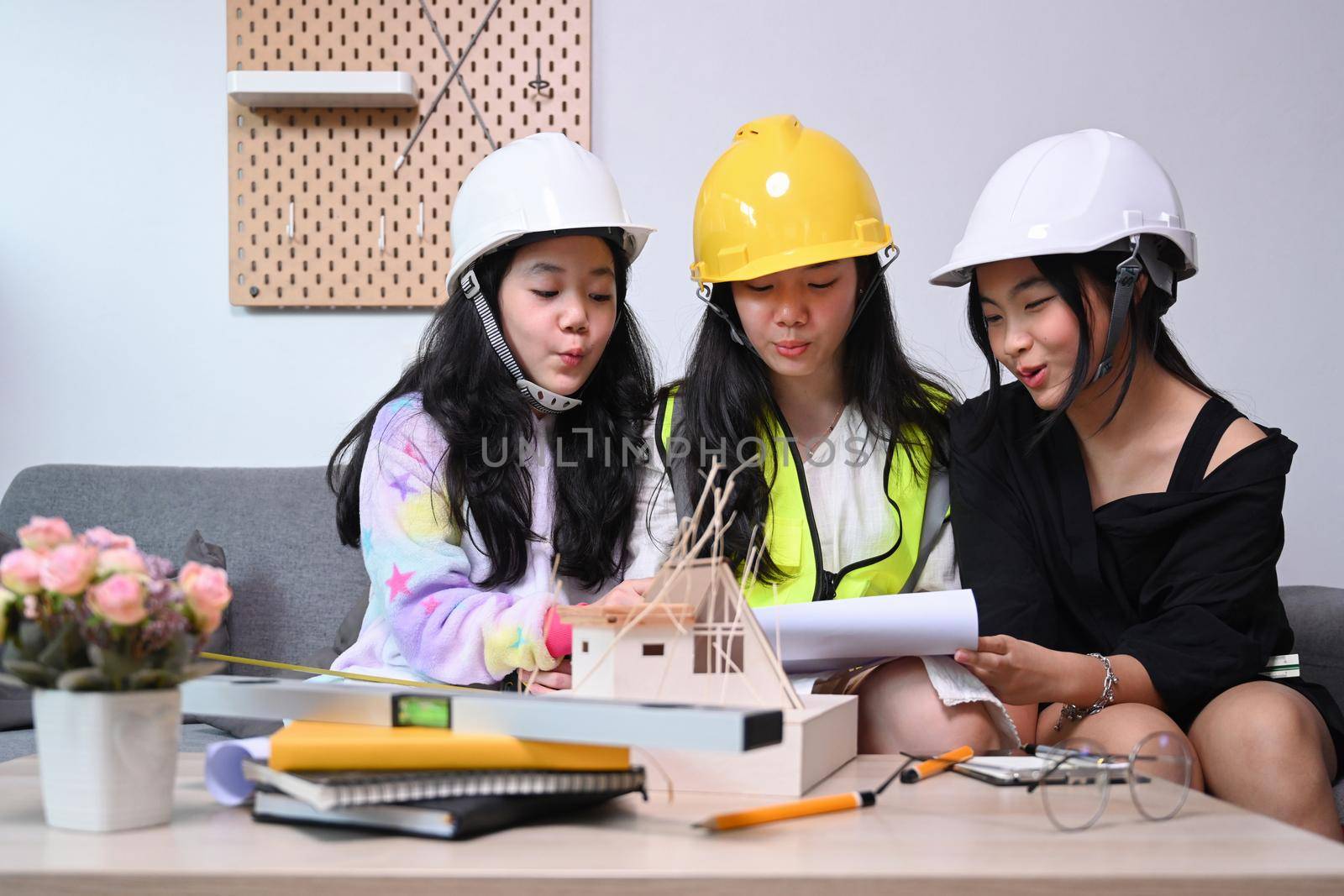 Three lovely asian girls in engineering uniform and safety helmet playing together at home. by prathanchorruangsak