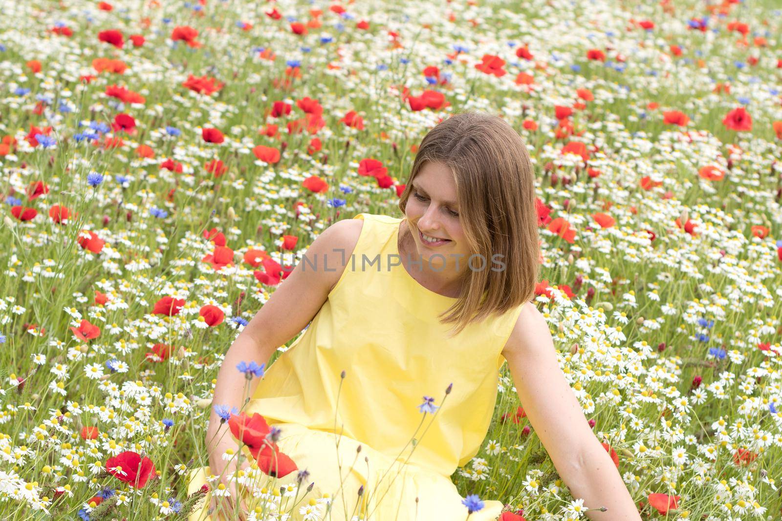 a beautiful young blonde woman in a yellow dress stands among a flowering field by KaterinaDalemans