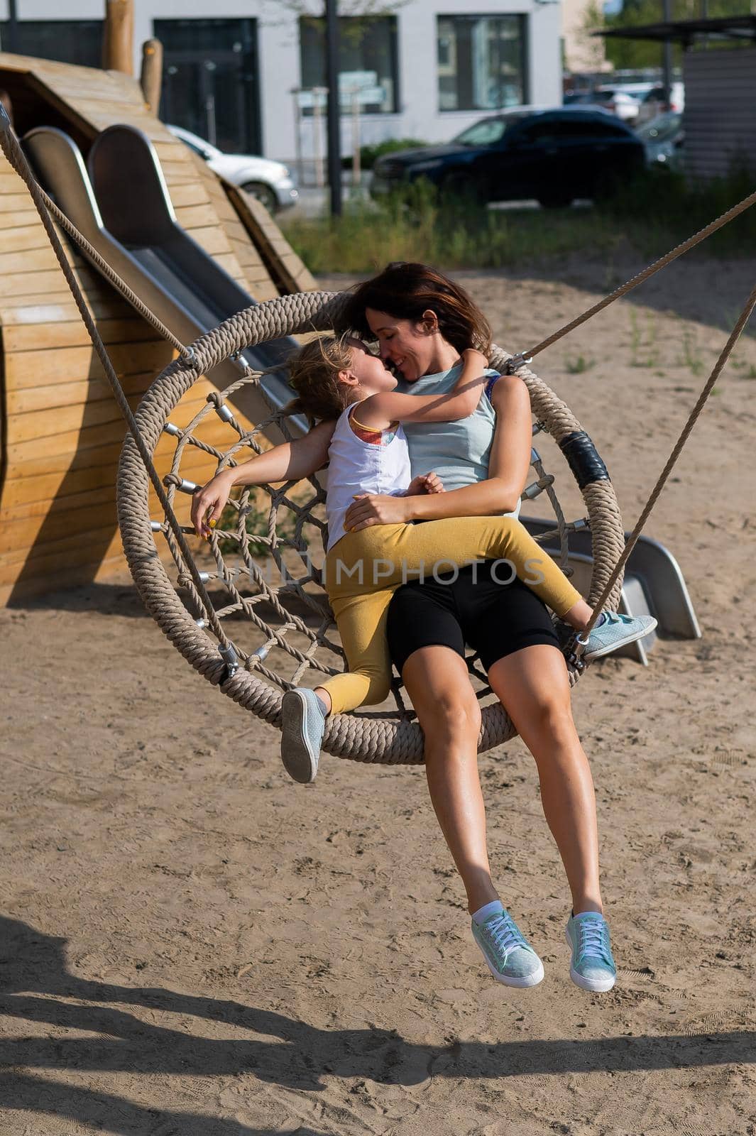 Mom and daughter swing on a round swing. Caucasian woman and little girl have fun on the playground