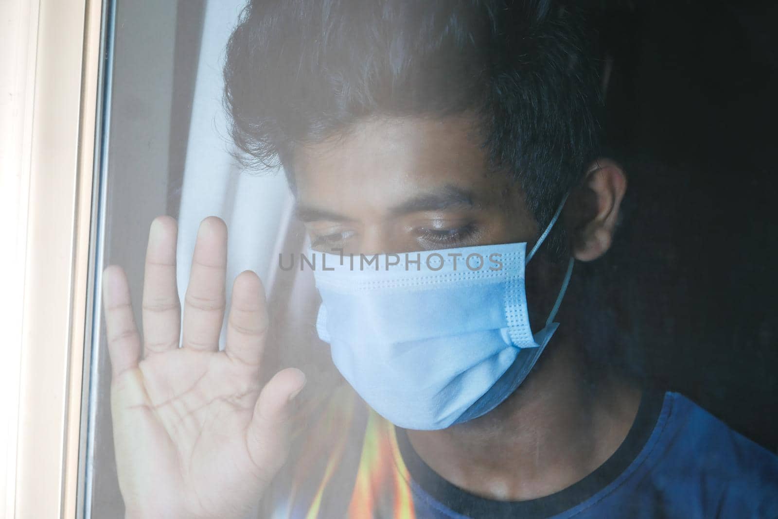 A young man with protective mask looking through window .