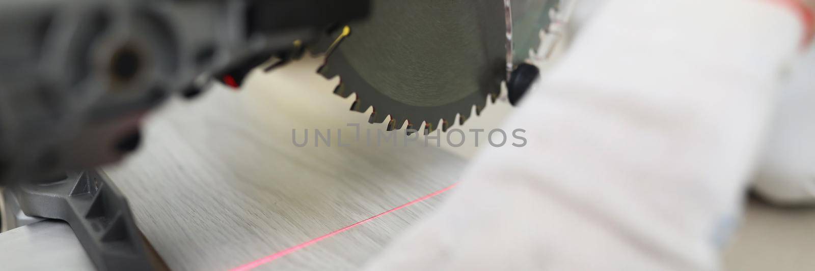 Close-up of red line of laser target pointer in place of future cut, hand of carpenter man controls saw instrument. Renovation, construction works, household repair concept