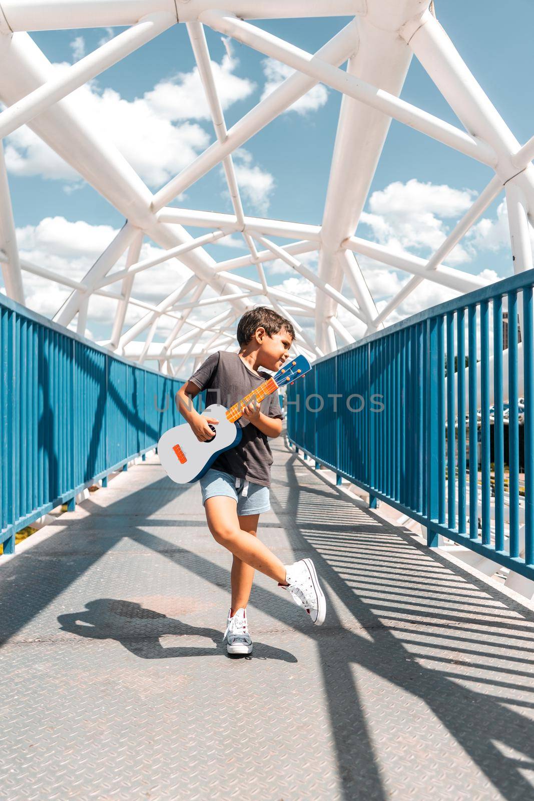 Latino boy posing with a ukulele cross-legged on a bridge in Managua Nicaragua