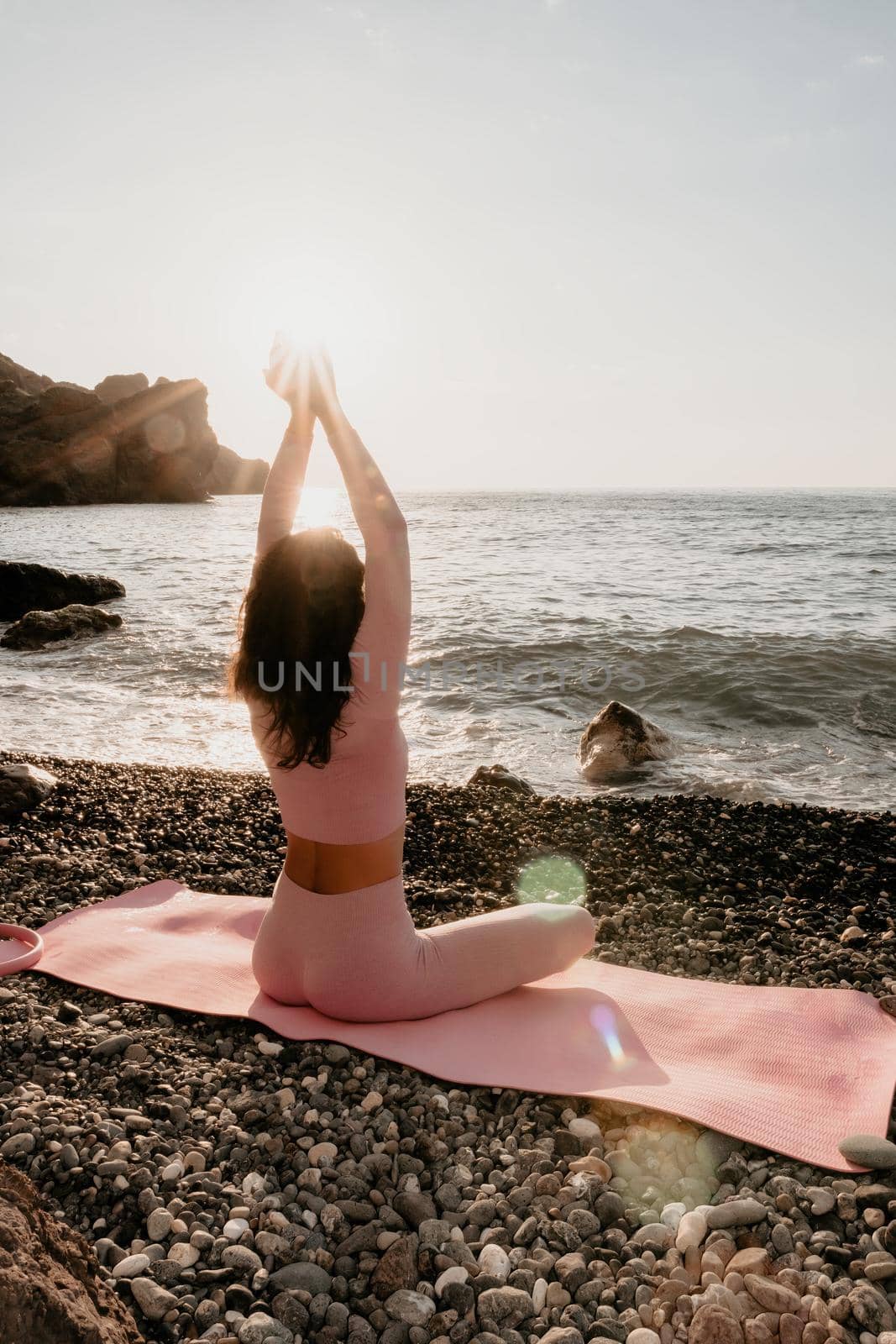 Young woman with black hair, fitness instructor in pink sports leggings and tops, doing pilates on yoga mat with magic pilates ring by the sea on the beach. Female fitness daily yoga concept