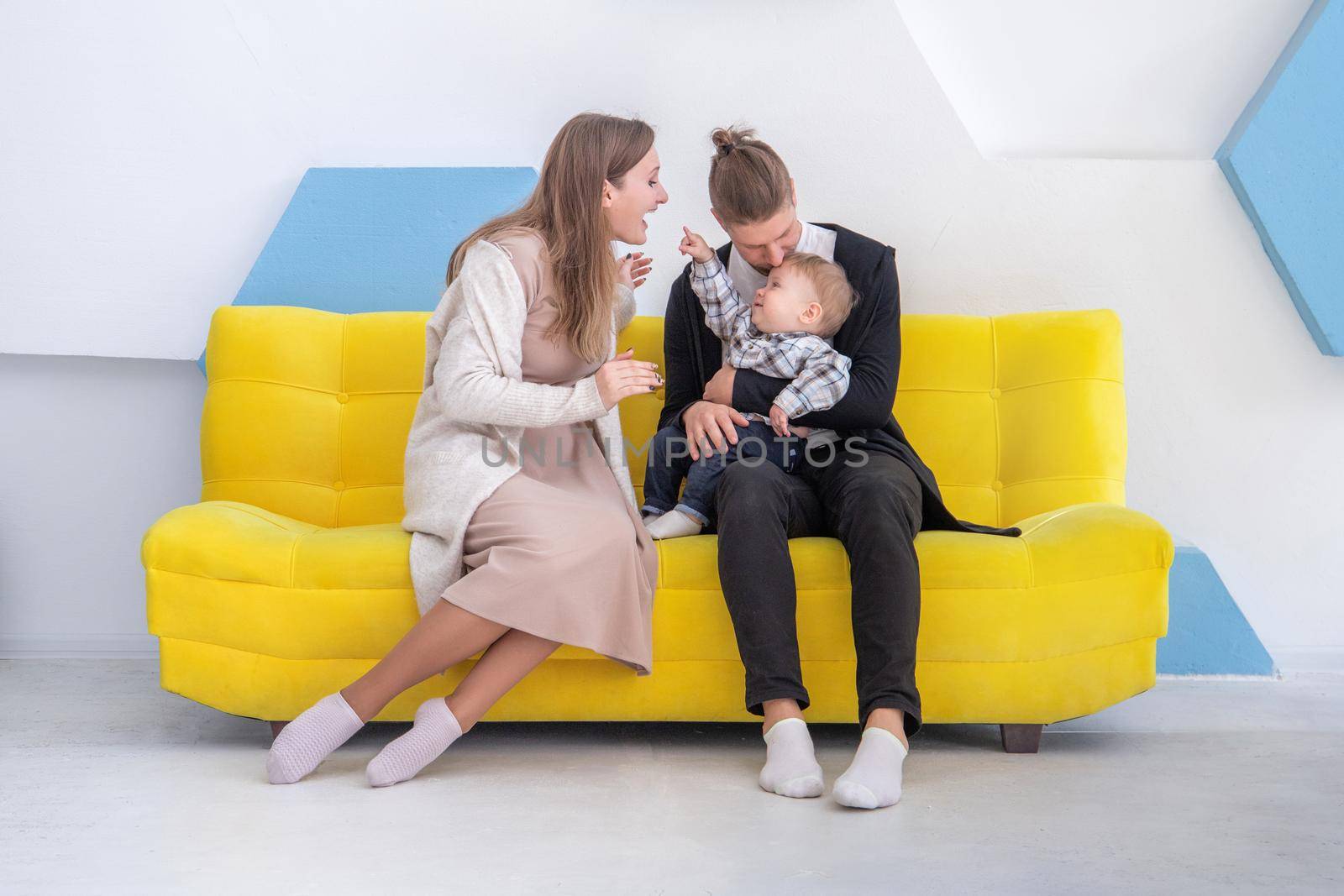 Little cute boy 1 year old spends time together with parents on yellow sofa.