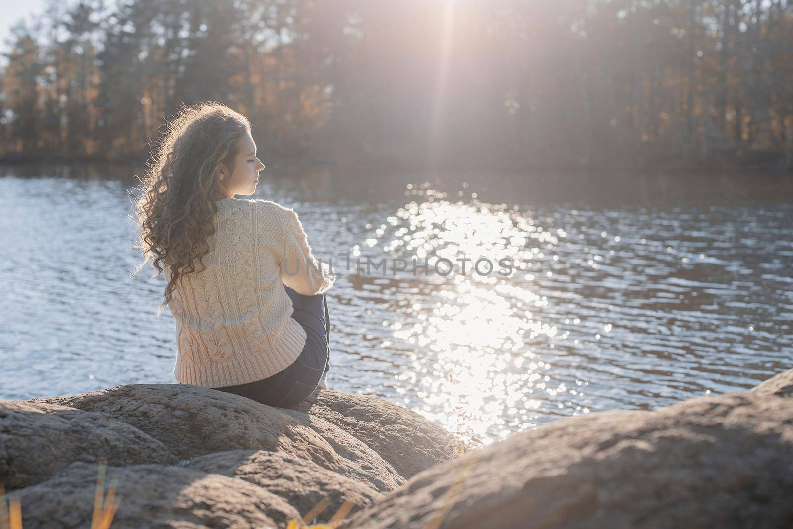 Thoughtful romantic woman sitting on the river bank in sunset in autumn day by Desperada