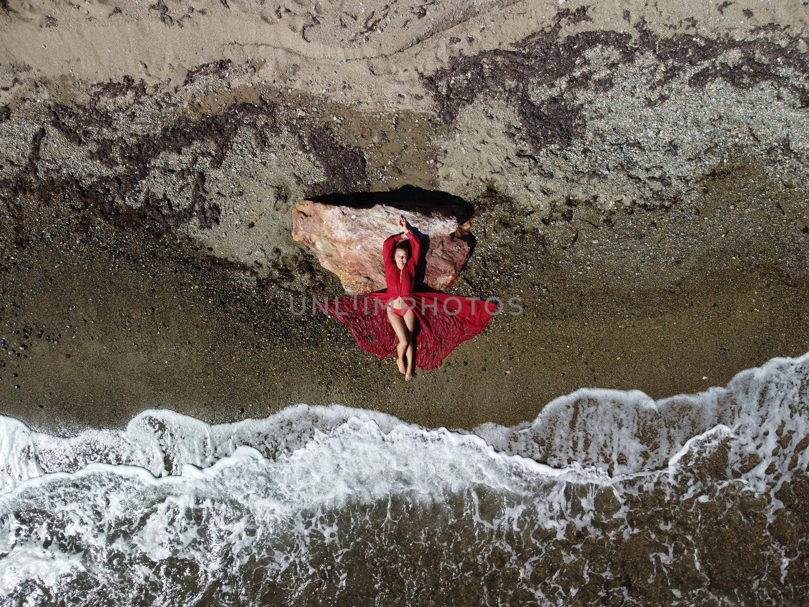 Young sensual blonde woman sitting on the rock near water at sea and enjoys the sea waves on background of two volcanic rocks, like in Iceland. Dreams holidays and weekend vacation in summer time