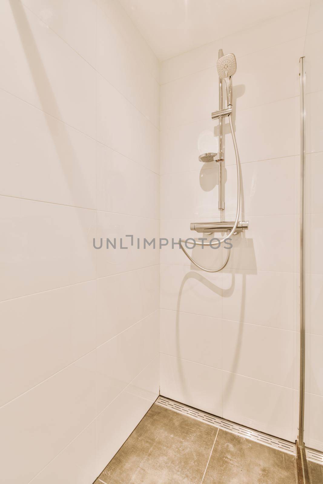 Shower faucets attached to tiled wall near glass partition and ornamental curtail in washroom at home