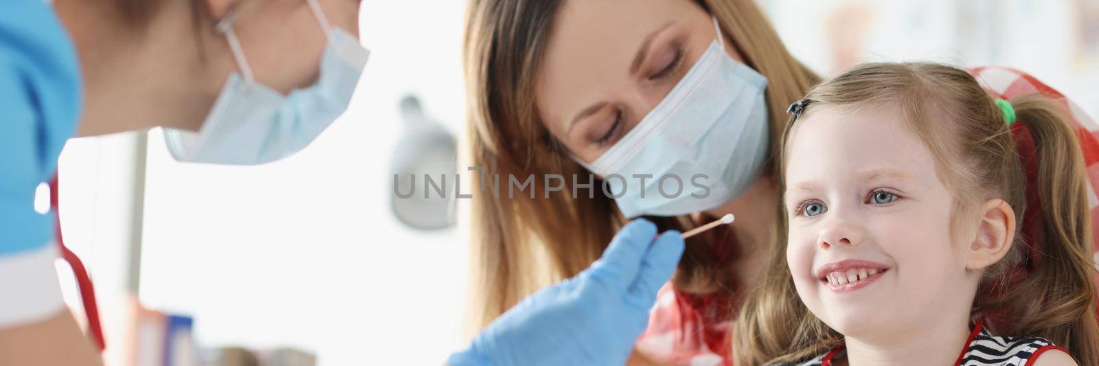 Portrait of doctor collects biological material from child saliva, coronavirus nasal swab test for kids. Little girl patient in hospital. Virus outbreak, analysis, checkup, medicine, health concept