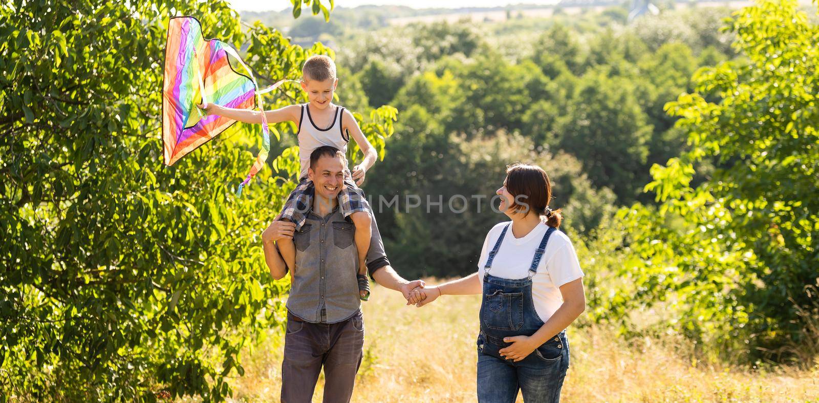 Happy family with pregnant wife fly a kite together in summer field