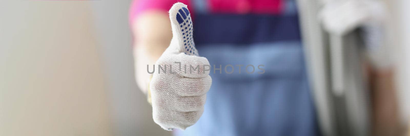 Close-up of woman hand demonstrating thumb up sign. Female repairer in coveralls. Motivational gesture. Repairs and renovation and repair home concept