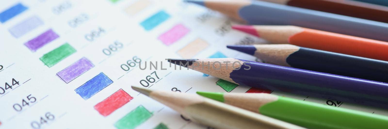 Close-up of bunch of pencils lay on paper with all listed colours. Big assortment of tools for drawing, develop creative vision, express yourself. Art, design, hobby, painting concept