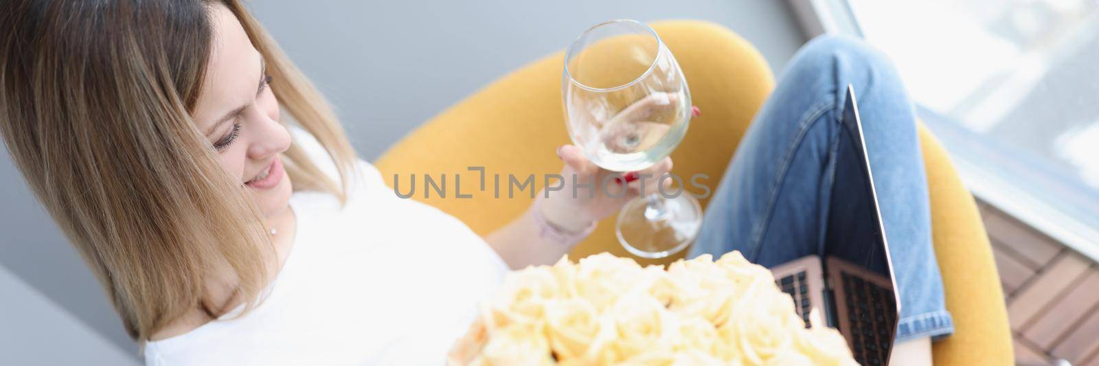 Portrait of blonde woman with luxury flowers, glass of wine work with laptop, celebrating birthday, delivery from courier. Freelancer, work from home, remote job, gift concept