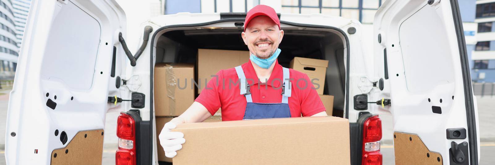 Portrait of smiling happy man unload truck and carry big cardboard package, courier in uniform deliver order to owner. Delivery service, worldwide shipping, dream job concept