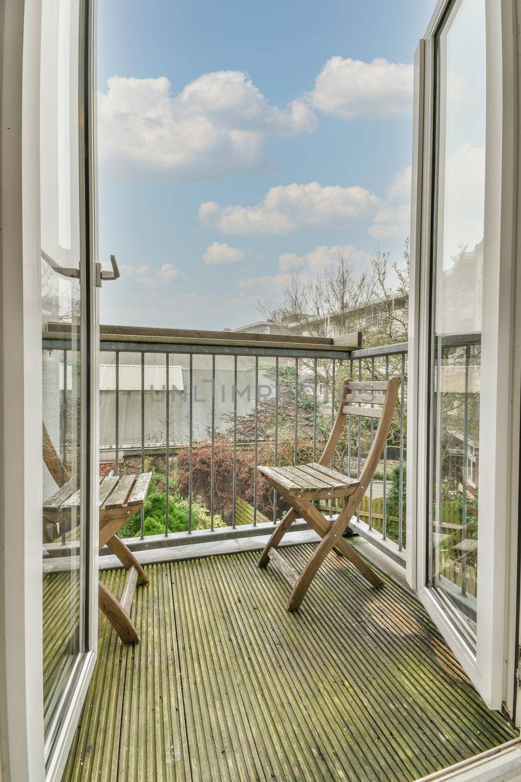 Narrow brick balcony with metal railings, wooden chair and door with glass leads to the kitchen