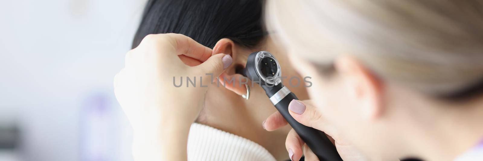 Close-up of female otolaryngologist examining ear with otoscope. Patient with earache at doctor appointment. Otolaryngology, medicine and healthcare concept