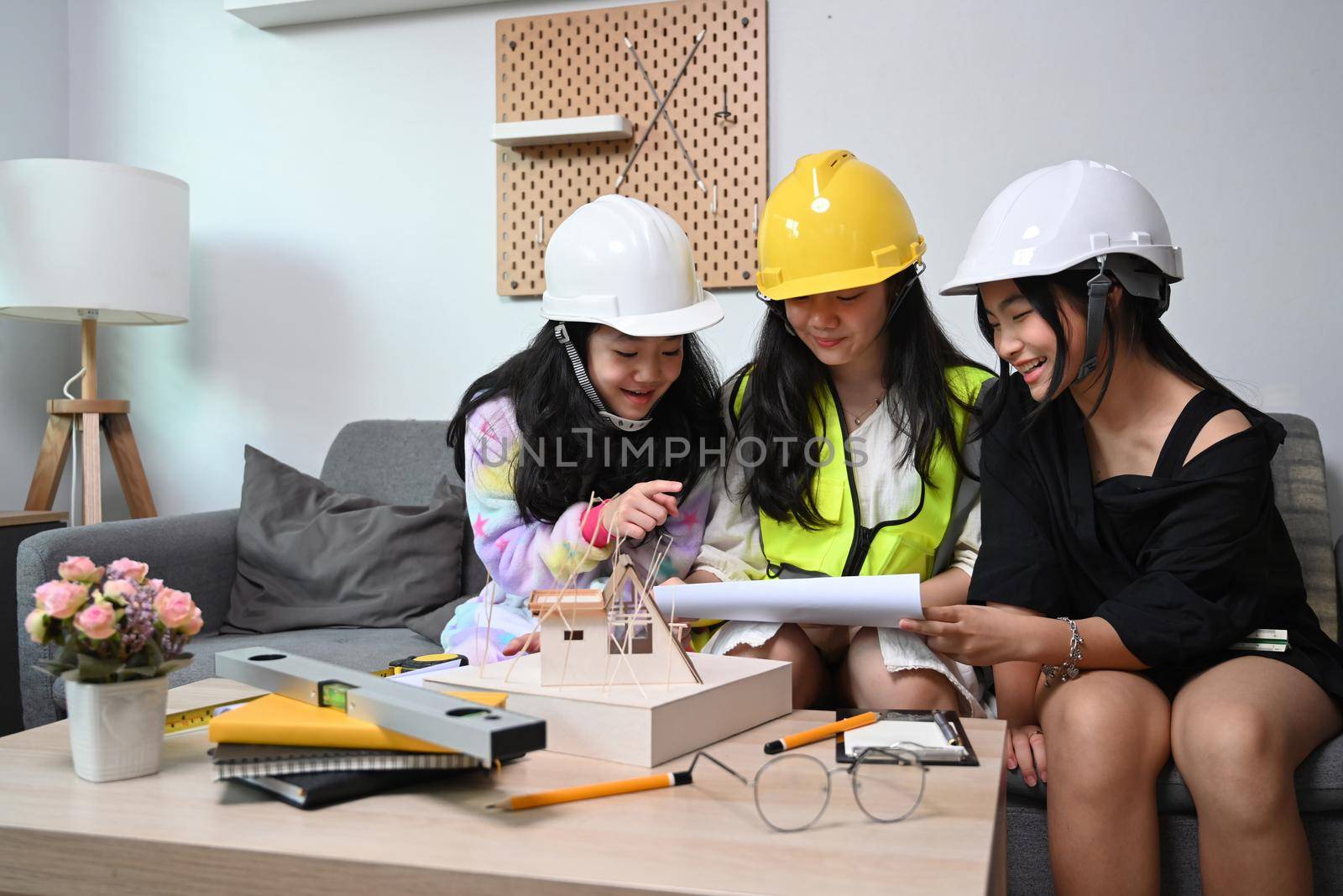 Three asian girls wearing hard hat while playing as engineer together at home.