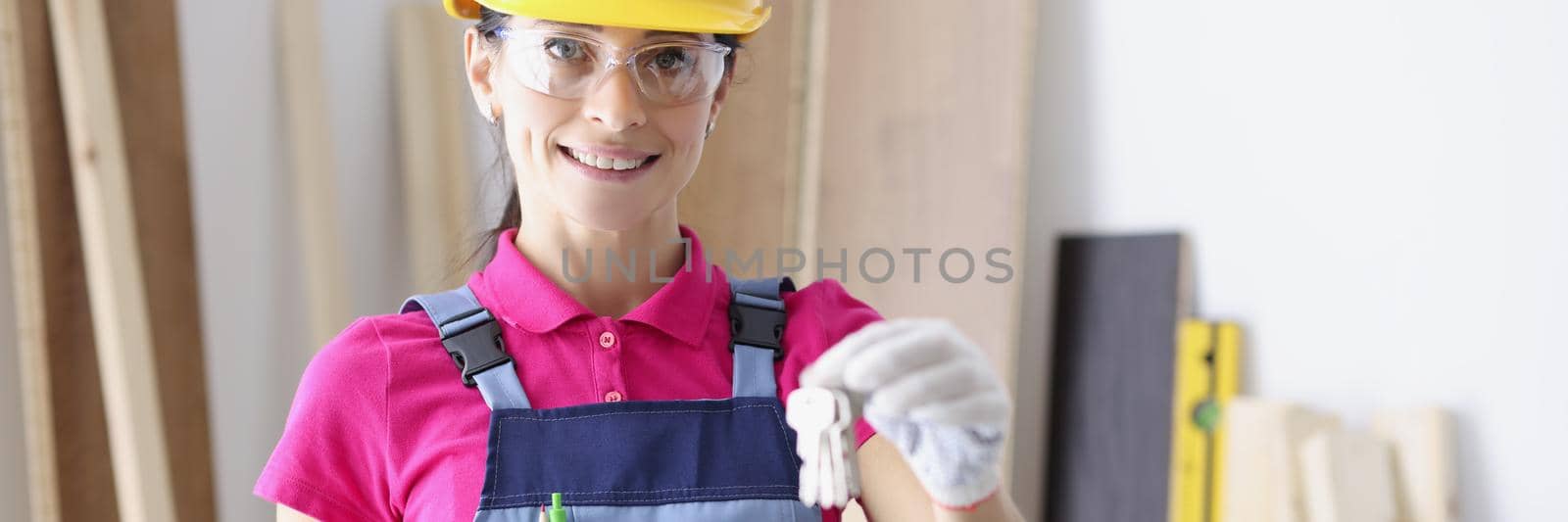 Portrait of smiling female builder holding bunch of keys and documents in hands. Young repairer looking at camera with gladness. Turnkey repair system concept
