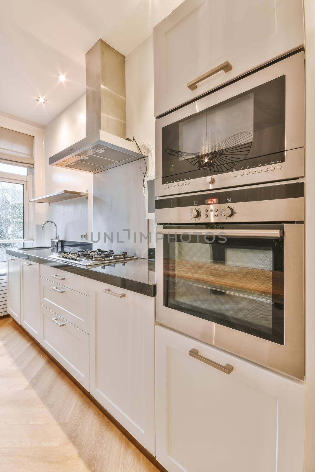 Fragment of interior of light narrow home kitchen with minimalist style white furniture with sink and stove