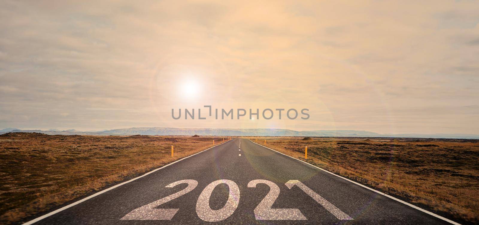 The word 2021 written on highway road in the middle of empty asphalt road at golden sunset and beautiful blue sky. High-quality photo