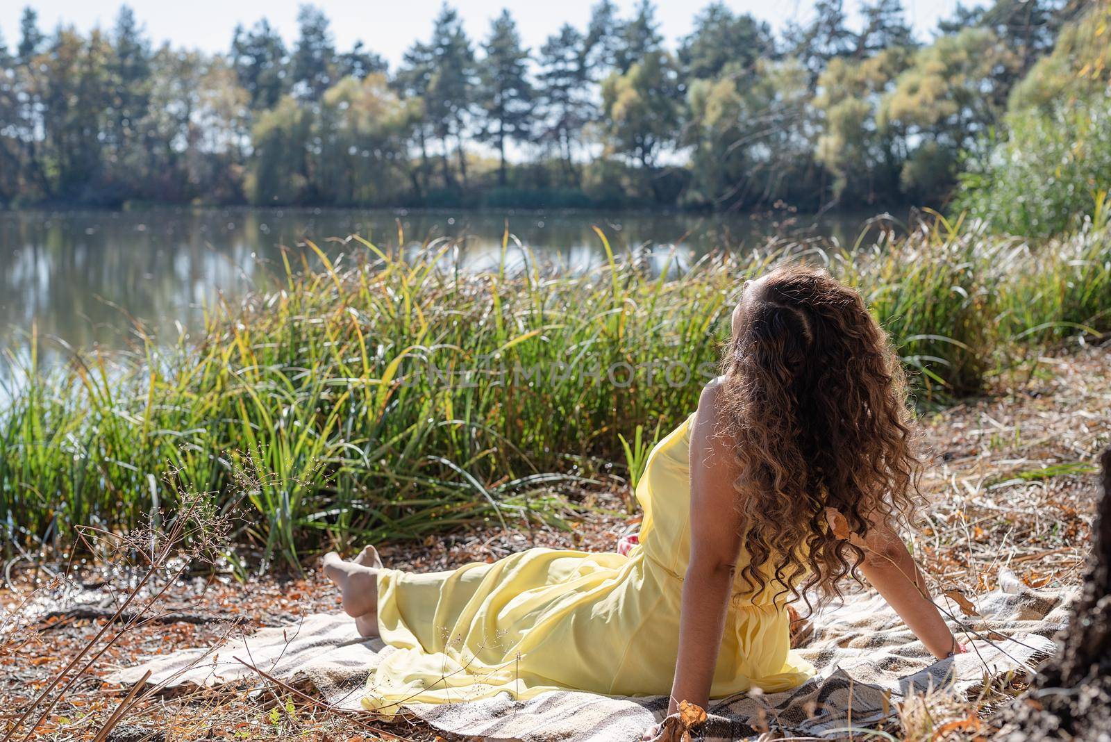 Leisure, free time. Beautiful caucasian woman in yellow dress on a picnic outdoors, sitting next to water