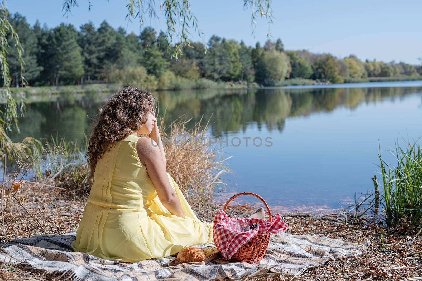 Leisure, free time. Beautiful caucasian woman in yellow dress on a picnic outdoors, sitting next to water