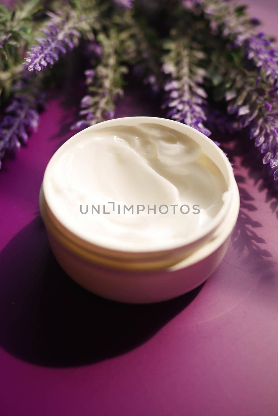 herbal cream cosmetic in a container and lavender flower on purple background .