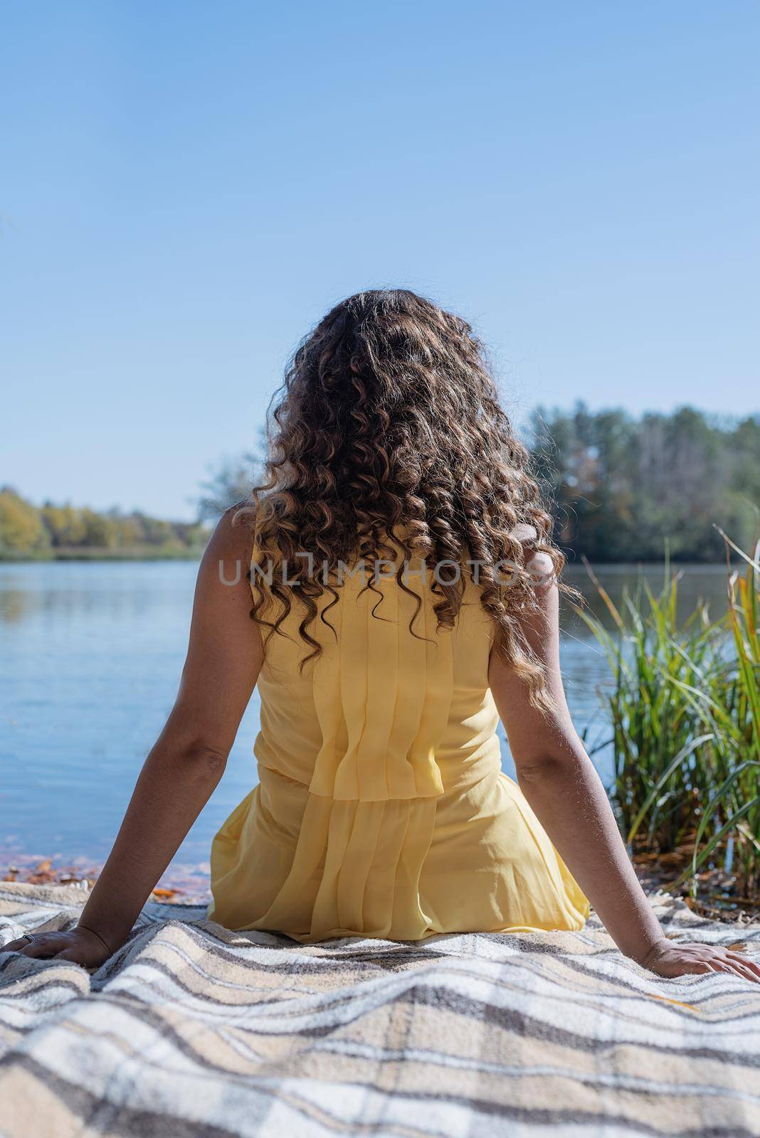 Leisure, free time. Beautiful caucasian woman in yellow dress on a picnic outdoors, sitting next to water