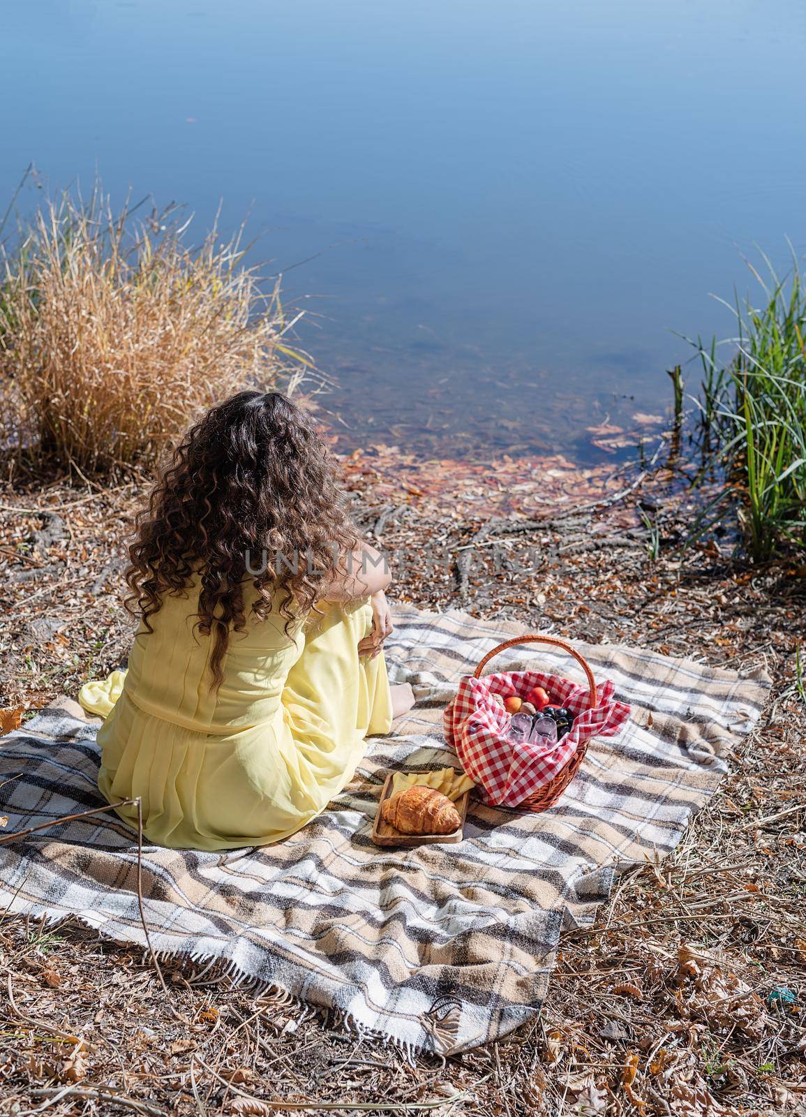 Leisure, free time. Beautiful caucasian woman in yellow dress on a picnic outdoors, sitting next to water