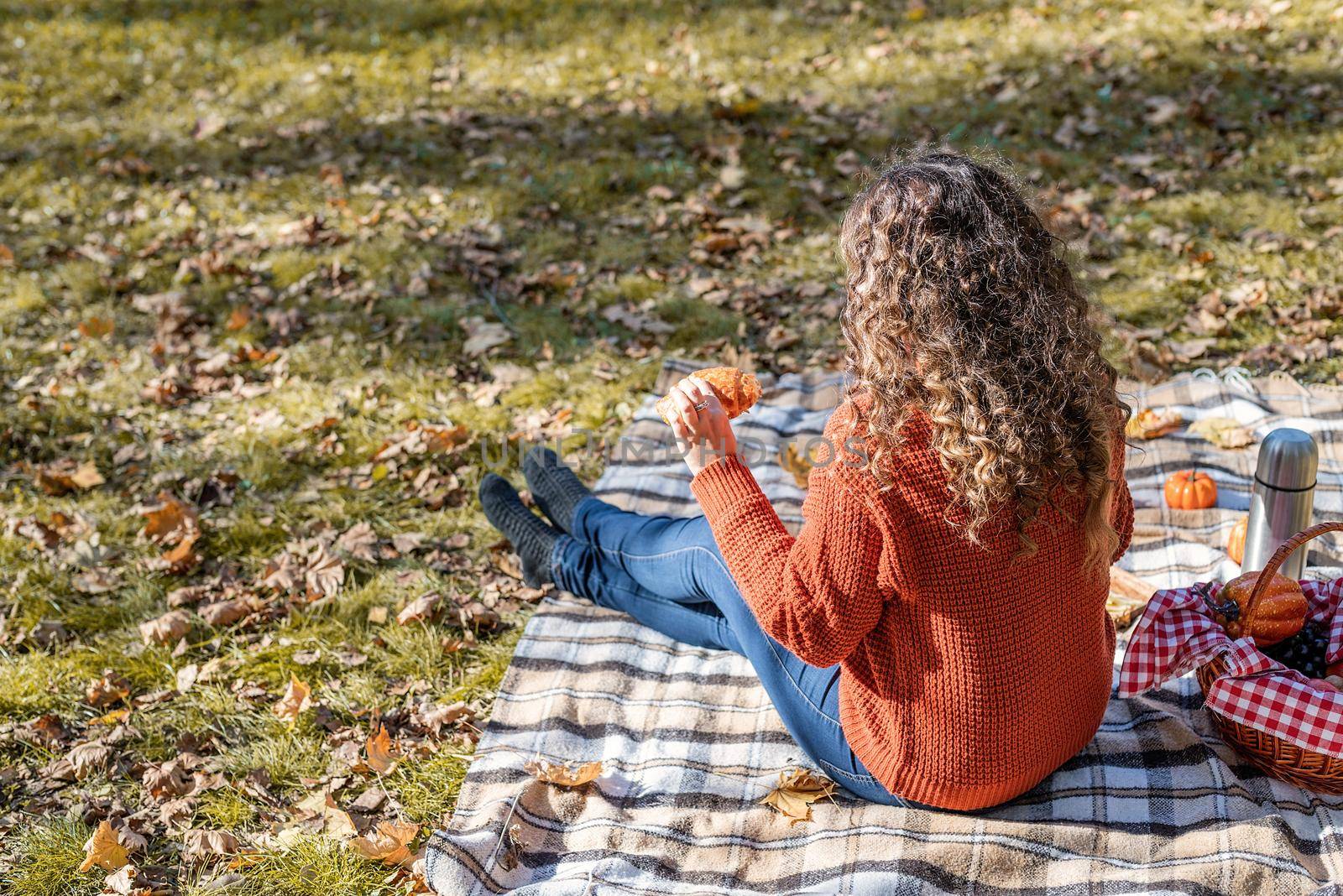 Leisure, free time. Beautiful caucasian woman in red sweater on a picnic outdoors, sitting on a plaid in autumn forest