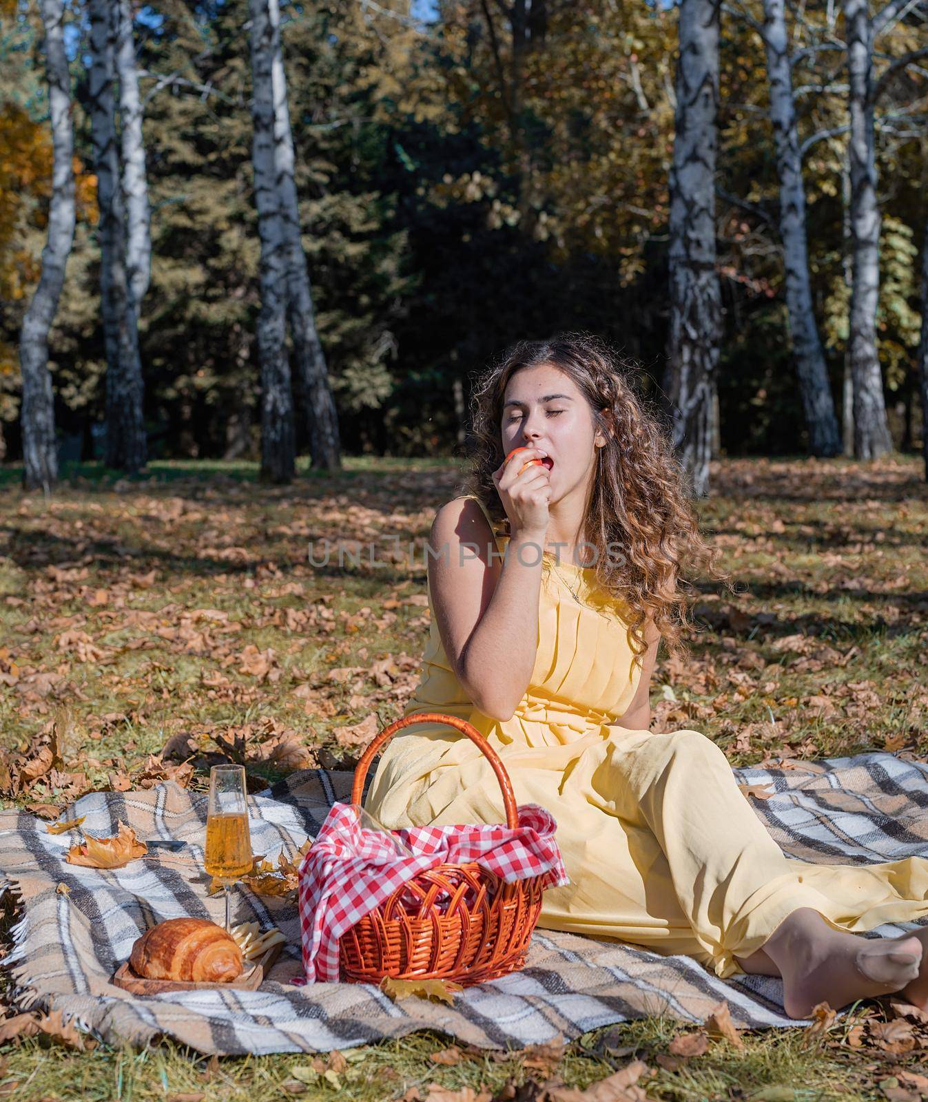 Leisure, free time. Beautiful caucasian woman in yellow dress on a picnic outdoors, sitting on a plaid in forest