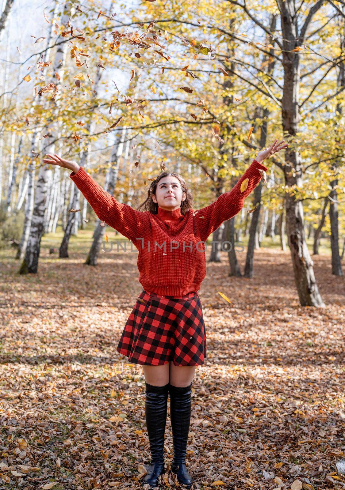 Autumn nature. Young happy woman in red sweater throwing leaves in autumn forest