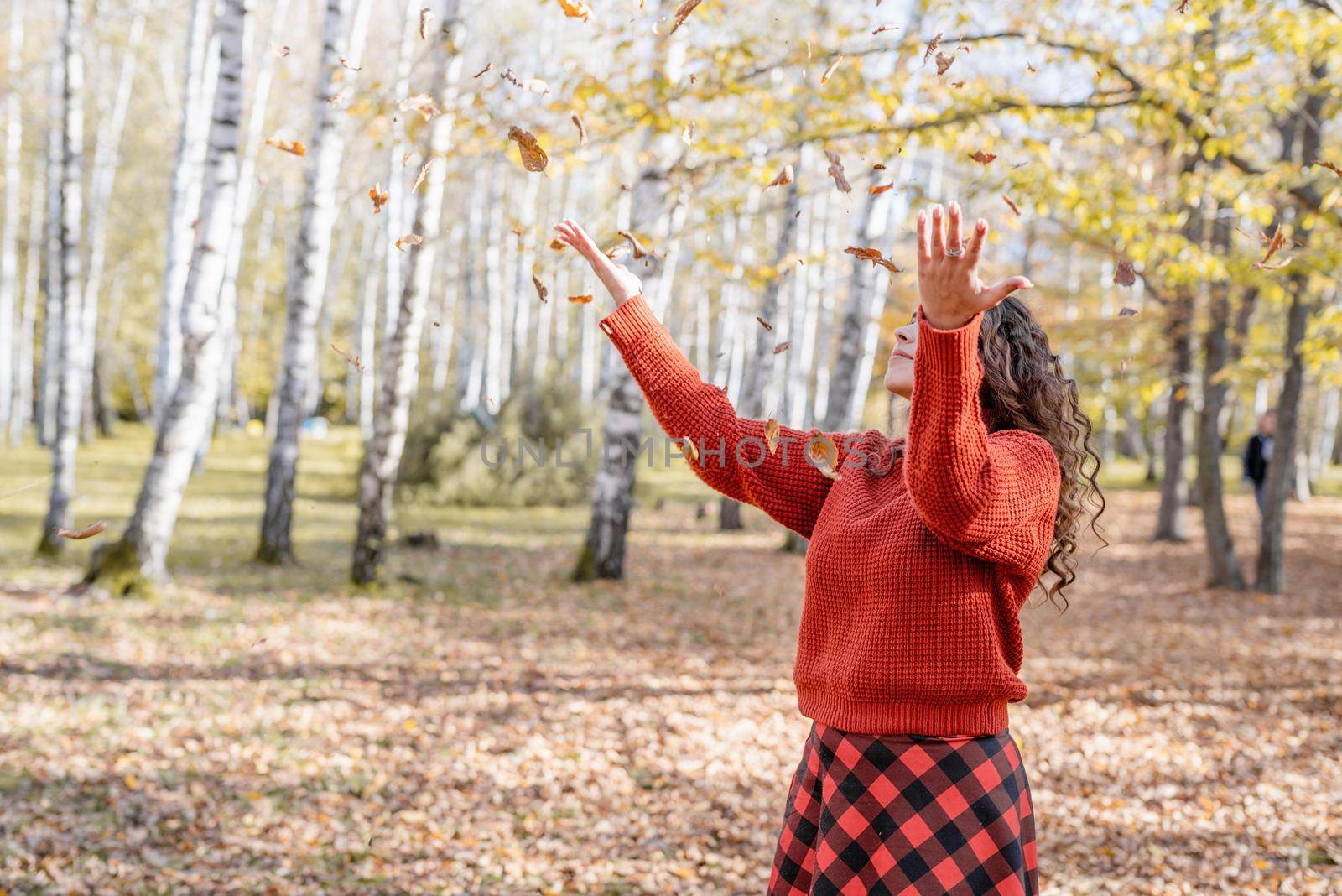 Autumn nature. Young happy woman in red sweater throwing leaves in autumn forest