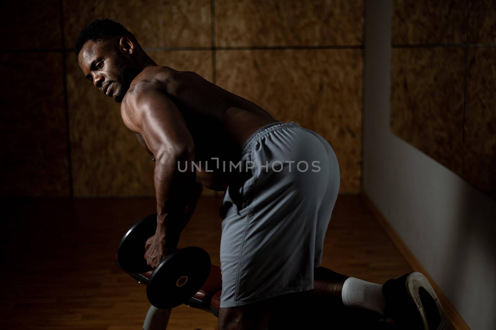 African american man with naked torso doing triceps row with dumbbell on bench