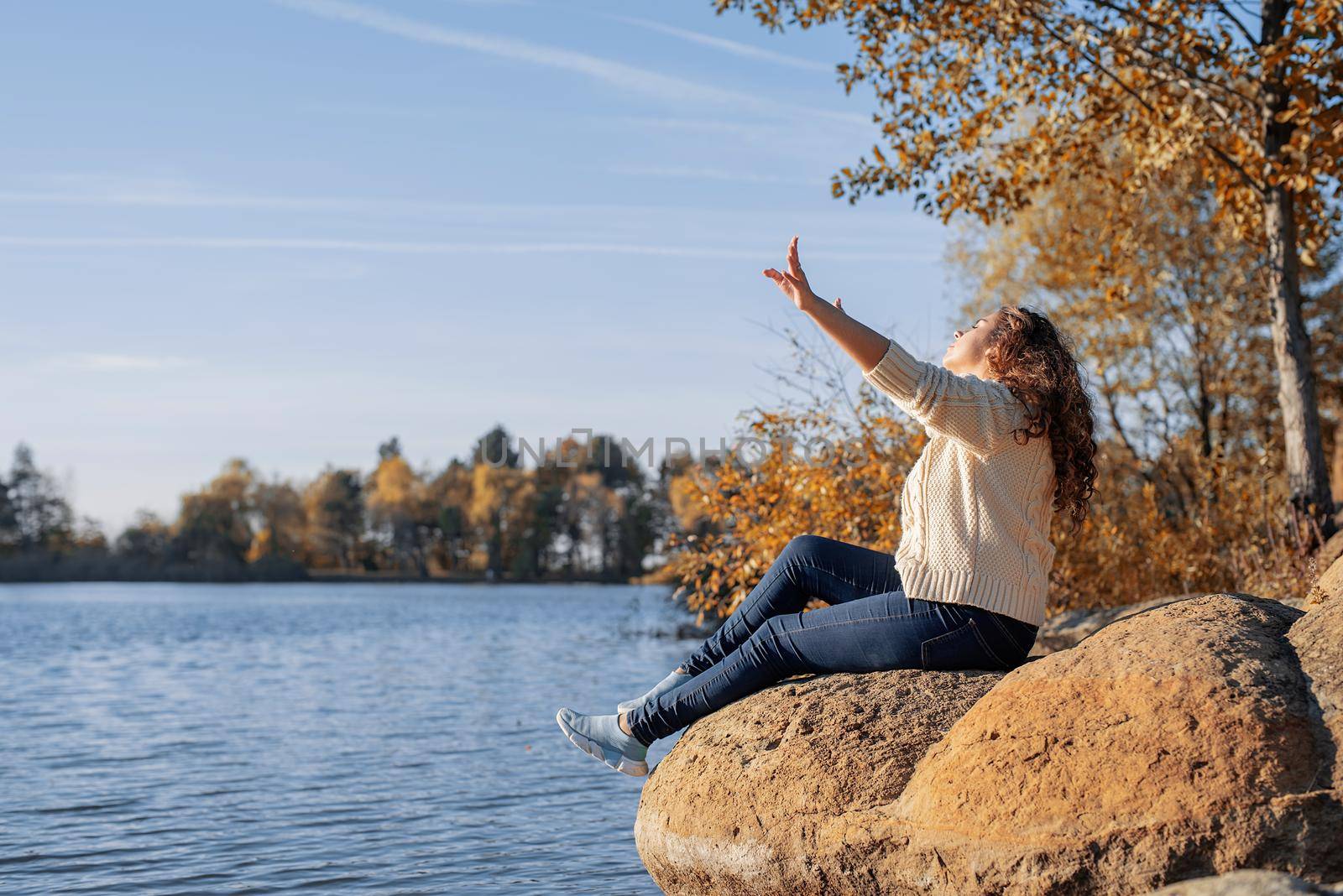 Thoughtful romantic woman sitting on rocks on the river bank in sunset in autumn day by Desperada