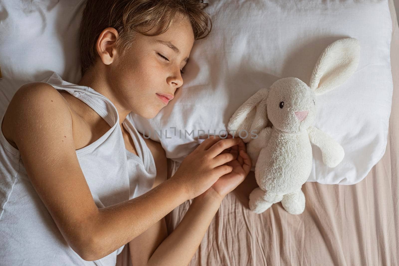 cute boy sleeping in bed. School child dreaming and holding plush toy.