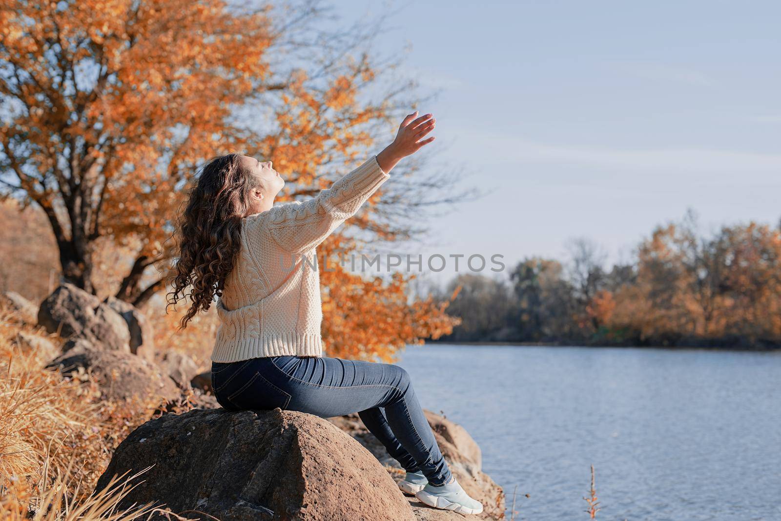 Freedom concept. Thoughtful romantic woman sitting on rocks on the river bank in sunset in autumn day, copy space.