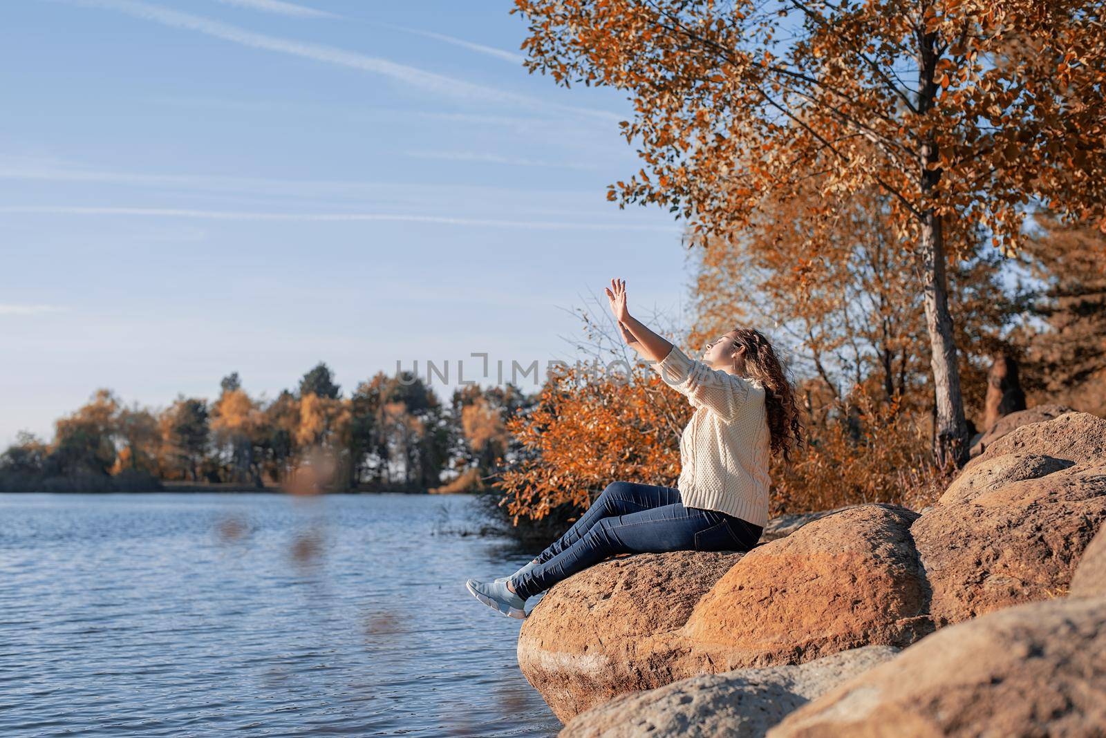 Freedom concept. Thoughtful romantic woman sitting on rocks on the river bank in sunset in autumn day, copy space.