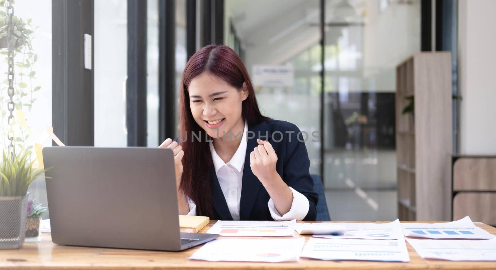 Beautiful Asian businesswoman celebrate while using laptop at office and showing delight. Startup small business and successful concept..