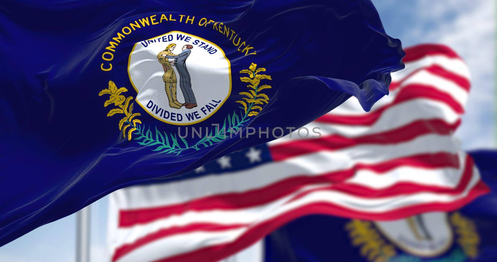 The Kentucky state flag waving along with the national flag of the United States of America. In the background there is a clear sky. Kentucky is a state in the Southeastern region of the United States