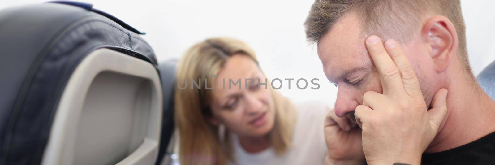 Portrait of male passenger having ear pop on airplane while taking off or landing, headache. Problem with sore head onboard. Fear of flying, agoraphobia, panic attacks concept