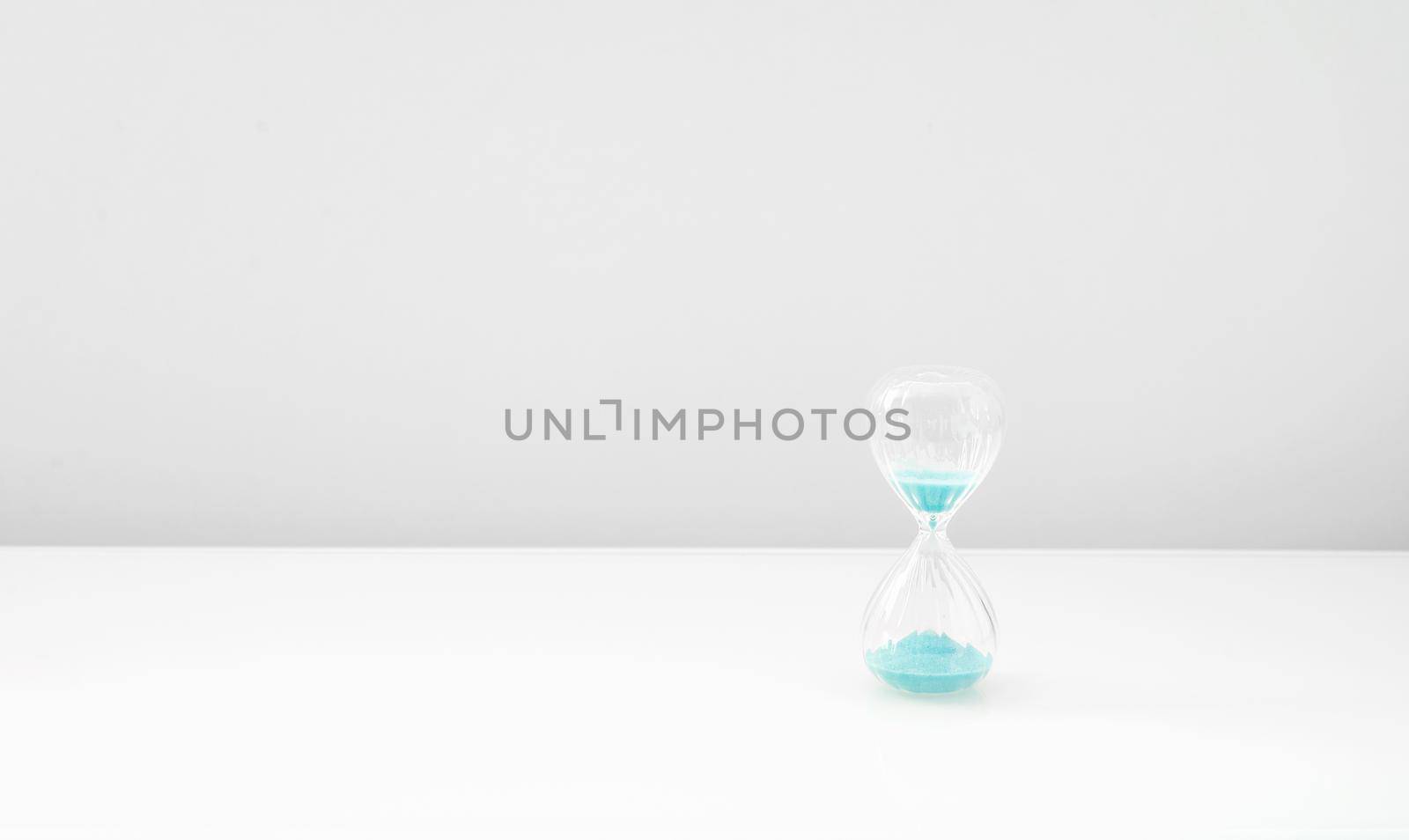 Hourglass on bright light, sandglass with blue sand  by ozornina