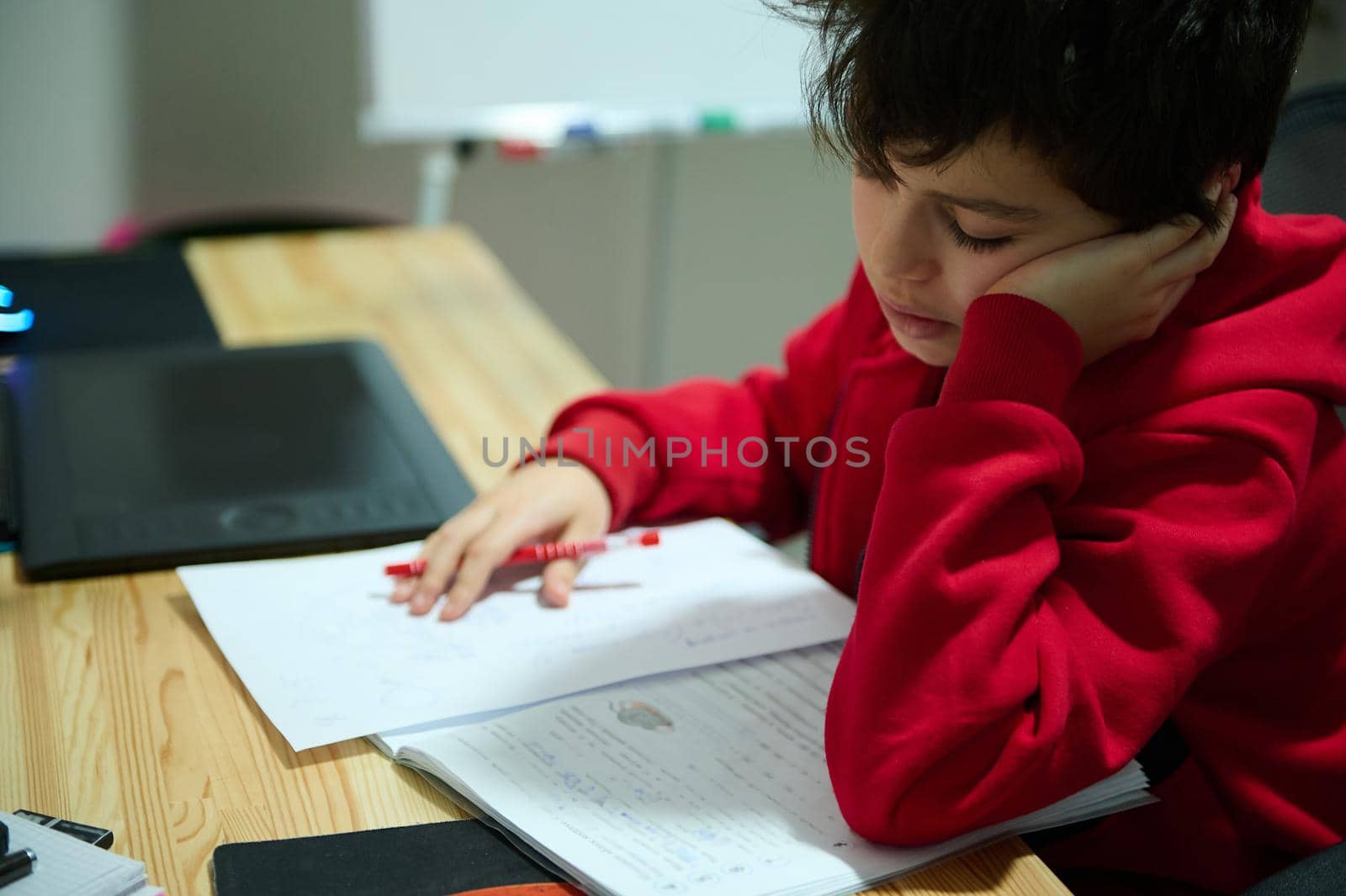 Adorable preadolescent Caucasian school boy sitting at wooden desk and concentrated on doing homework. Education, school life, erudition, knowledge concept. Back to school concept,education.