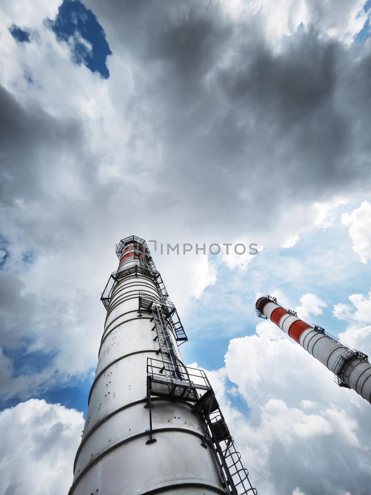 White chimneys of a power plant on a background of clouds with diagonal lines in a vertical frame