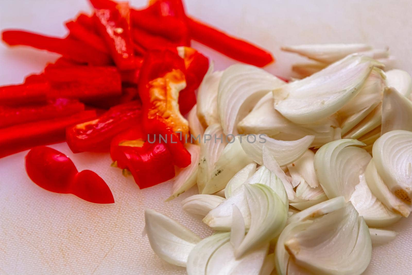 Wooden board with chopped vegetables: bell peppers, onions and parsley on light gray textured background, cooking, top view.