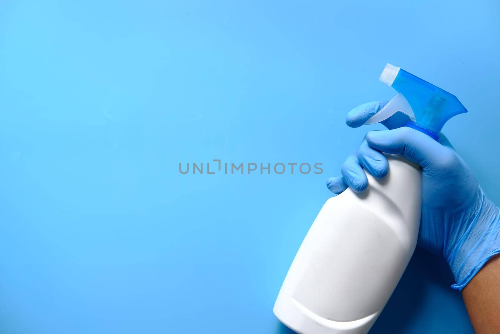 hand in blue rubber gloves holding spray bottle with copy space, top view