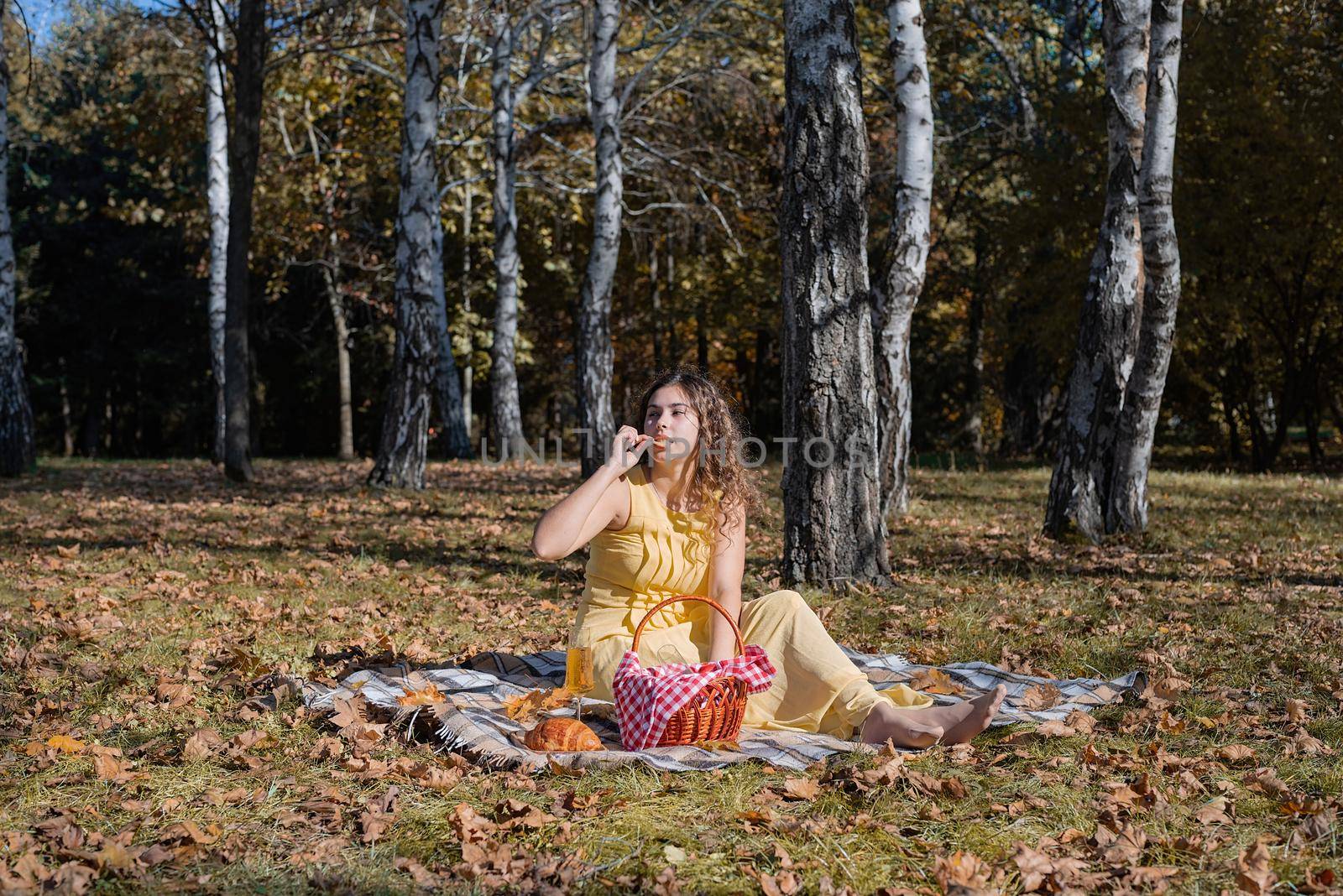 Leisure, free time. Beautiful caucasian woman in yellow dress on a picnic outdoors, sitting on a plaid in forest