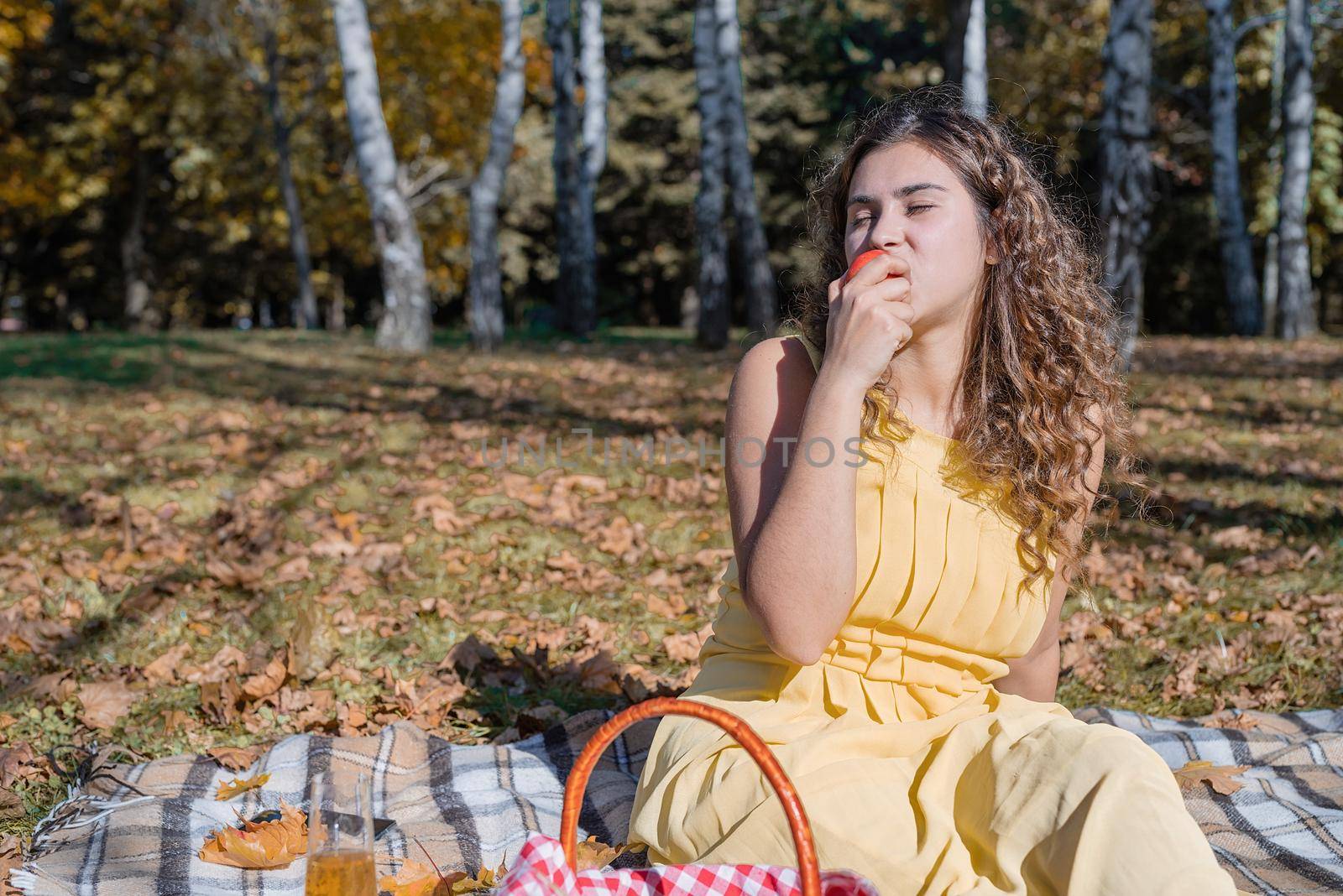 Leisure, free time. Beautiful caucasian woman in yellow dress on a picnic outdoors, sitting on a plaid in forest